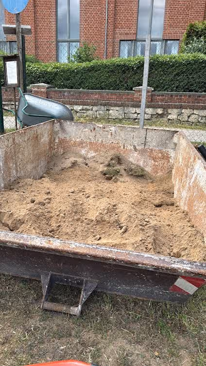 Anhänger mit ausgehobenem Sand, daneben Schubkarre auf der Straße