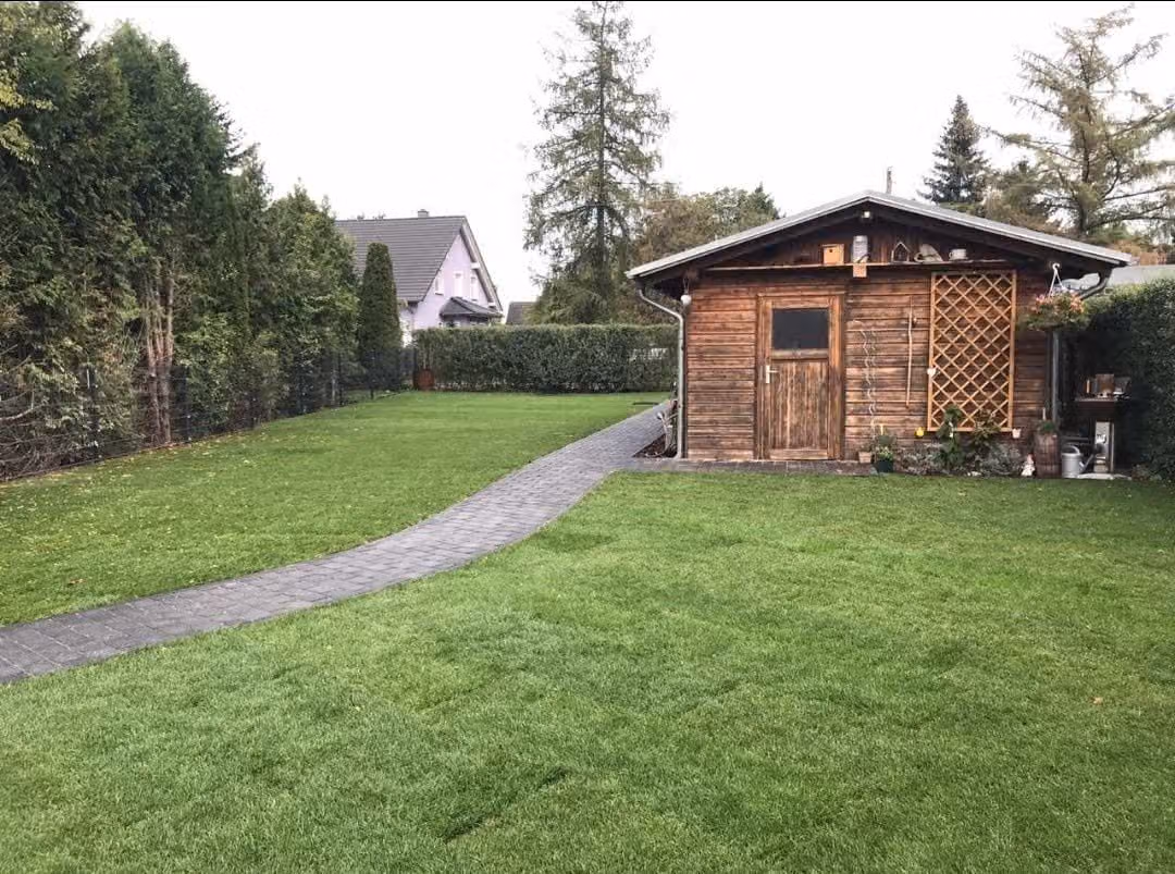 Geschwungener Pflasterweg über den Rasen zum Gartenhaus mit Carport
