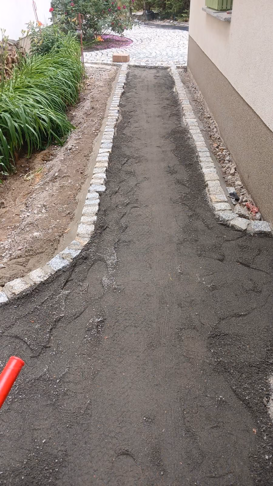 Gartenweg im Aufbau: verdichtetes Splittbett zwischen zwei Granit-Kleinpflasterkanten