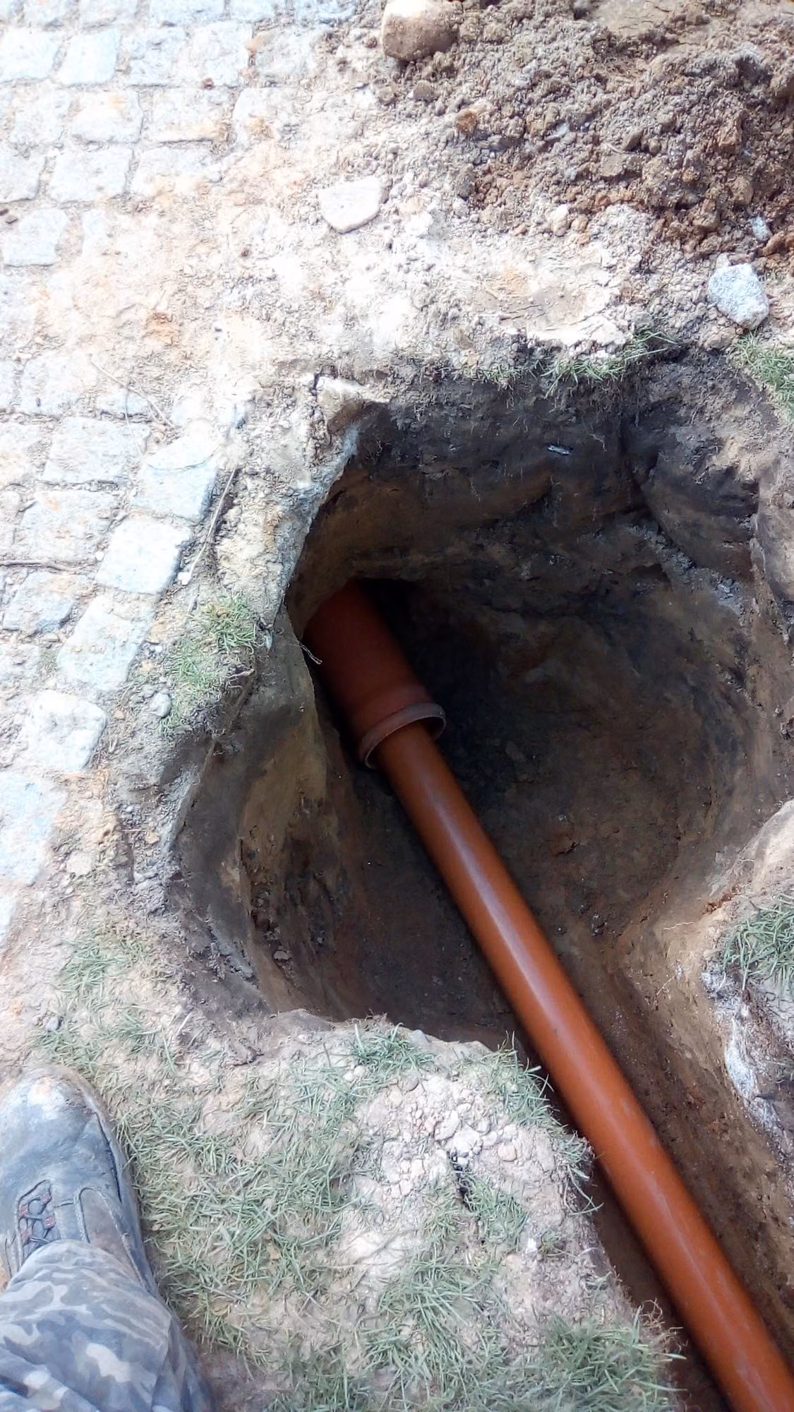 KG-Rohr-Anschluss in der Baugrube neben einem Natursteinpflasterweg