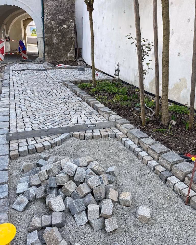 Mosaikpflasterweg mit gleichmäßiger Baumreihe entlang einer Grünfläche