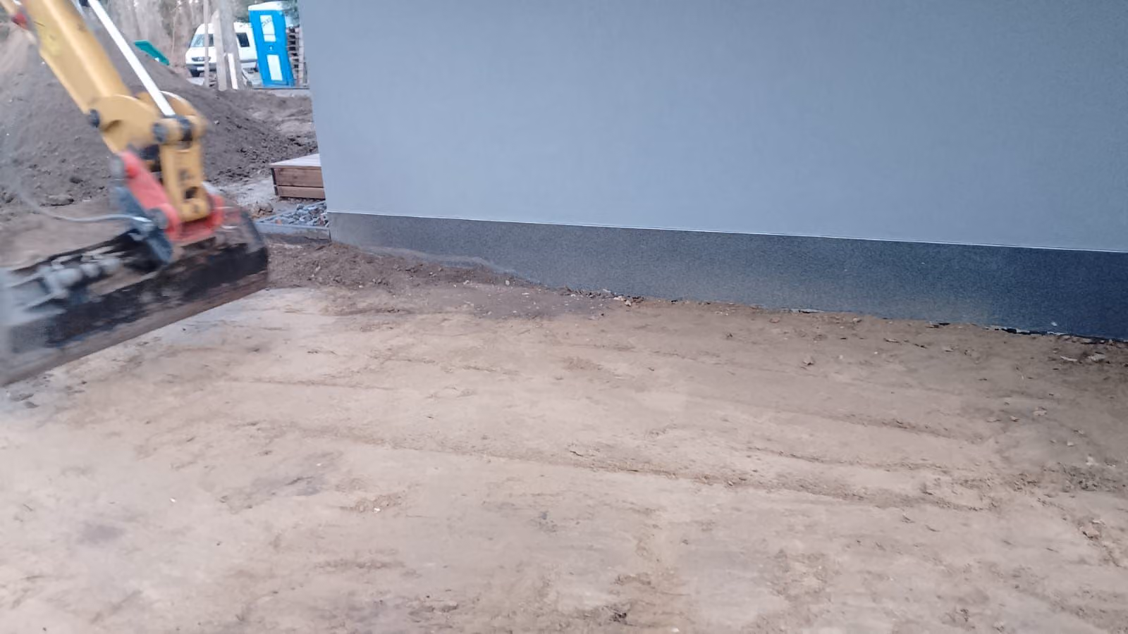 Bagger hebt den künftigen Weg an der Hausfassade aus