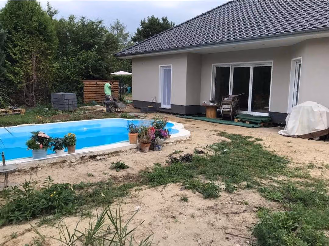 Poolbecken im Rohbau, umgeben von Sandfläche und Baumaterial