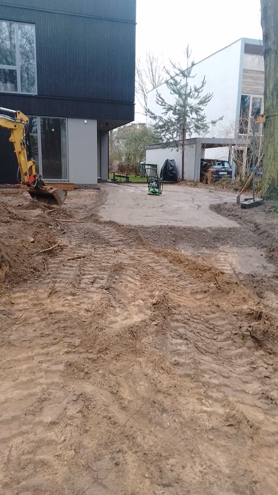 Verdichtete Zufahrt zwischen zwei Gebäuden mit Rüttelplatte und Bagger